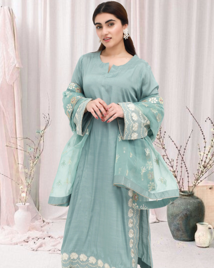 Daiselle-Woman wearing a light blue traditional outfit with floral patterns in a minimalistic setting.