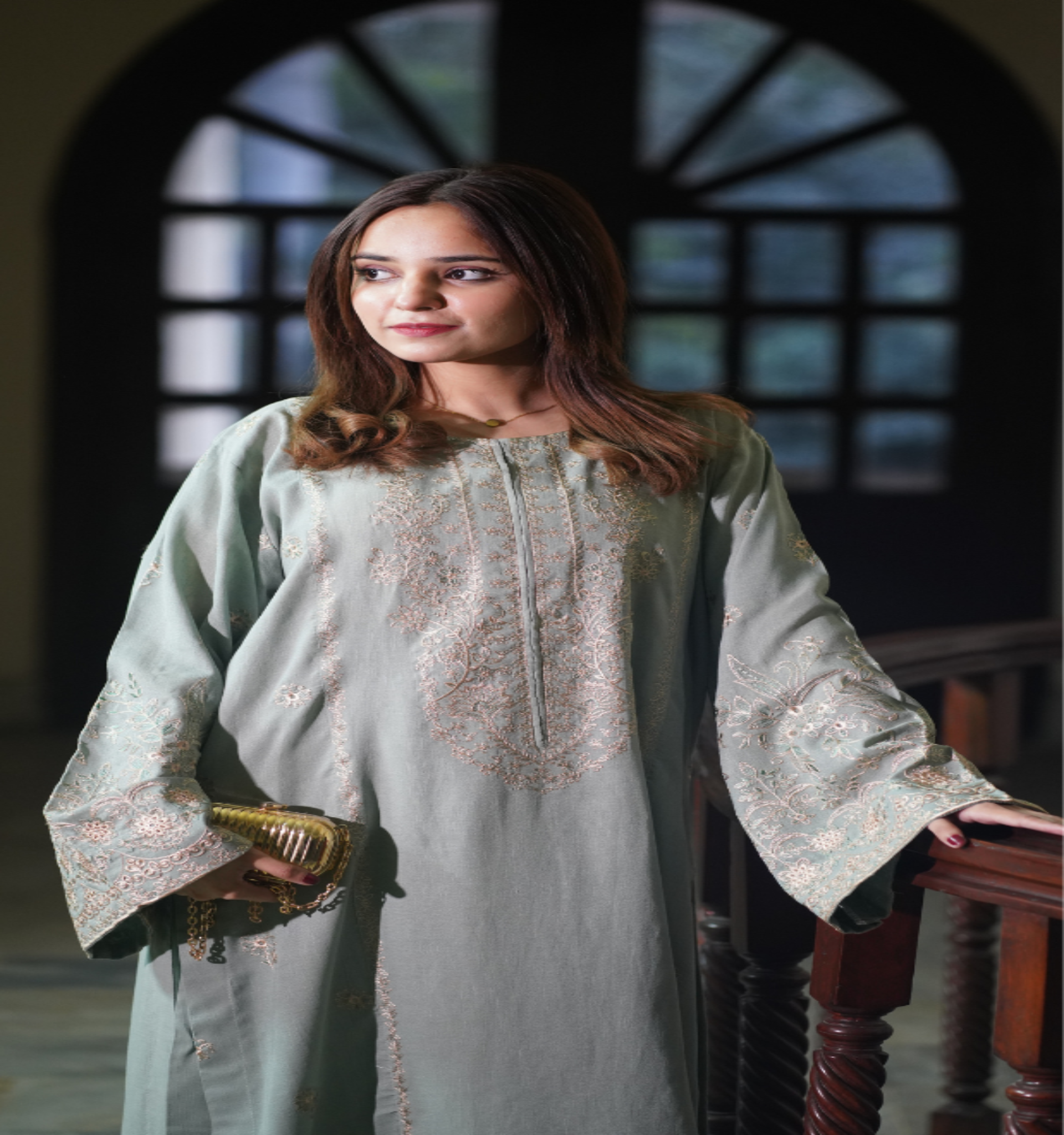 Woman wearing a light green traditional outfit with intricate patterns, standing indoors.